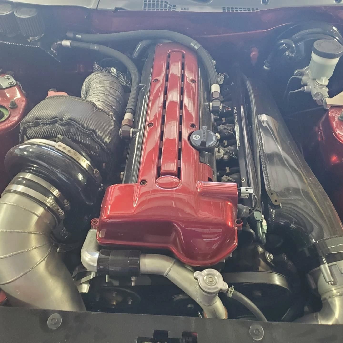 Custom car engine bay with a red valve cover and large polished turbo piping
