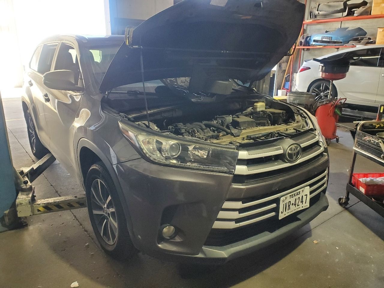 Gray SUV with hood open in a garage, showing the front end during maintenance.