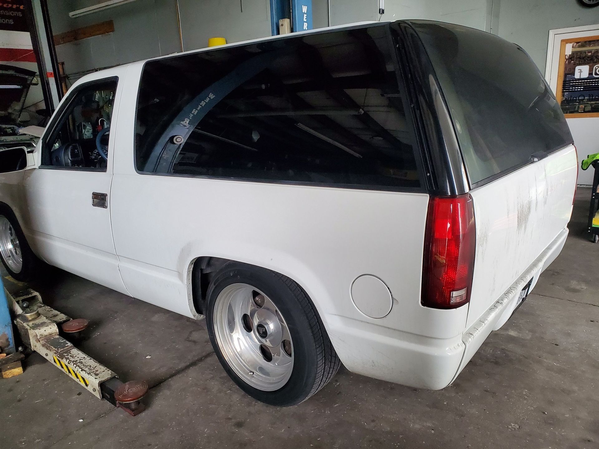 White SUV with a black canopy parked in a garage, viewed from the rear side.