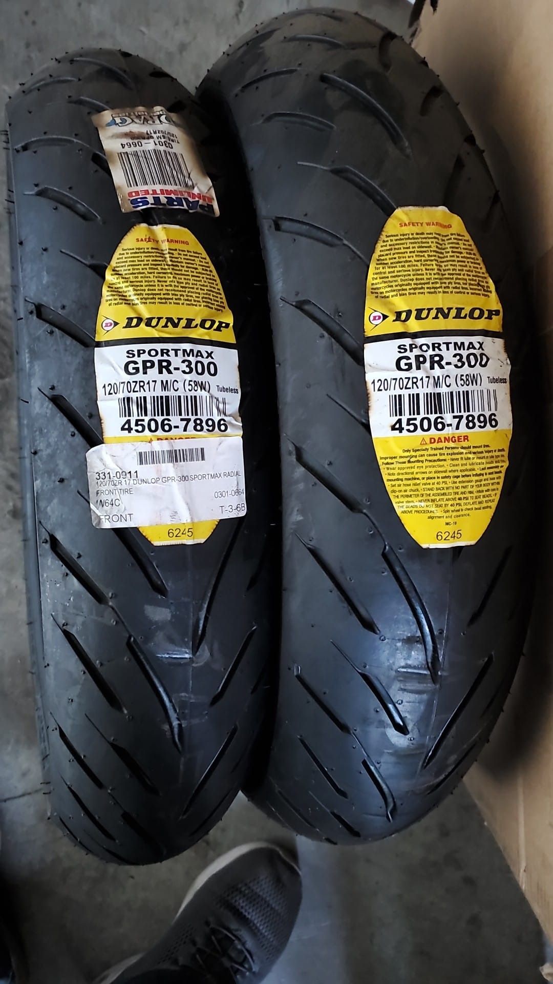 Two new black motorcycle tires with yellow and white labels on a floor