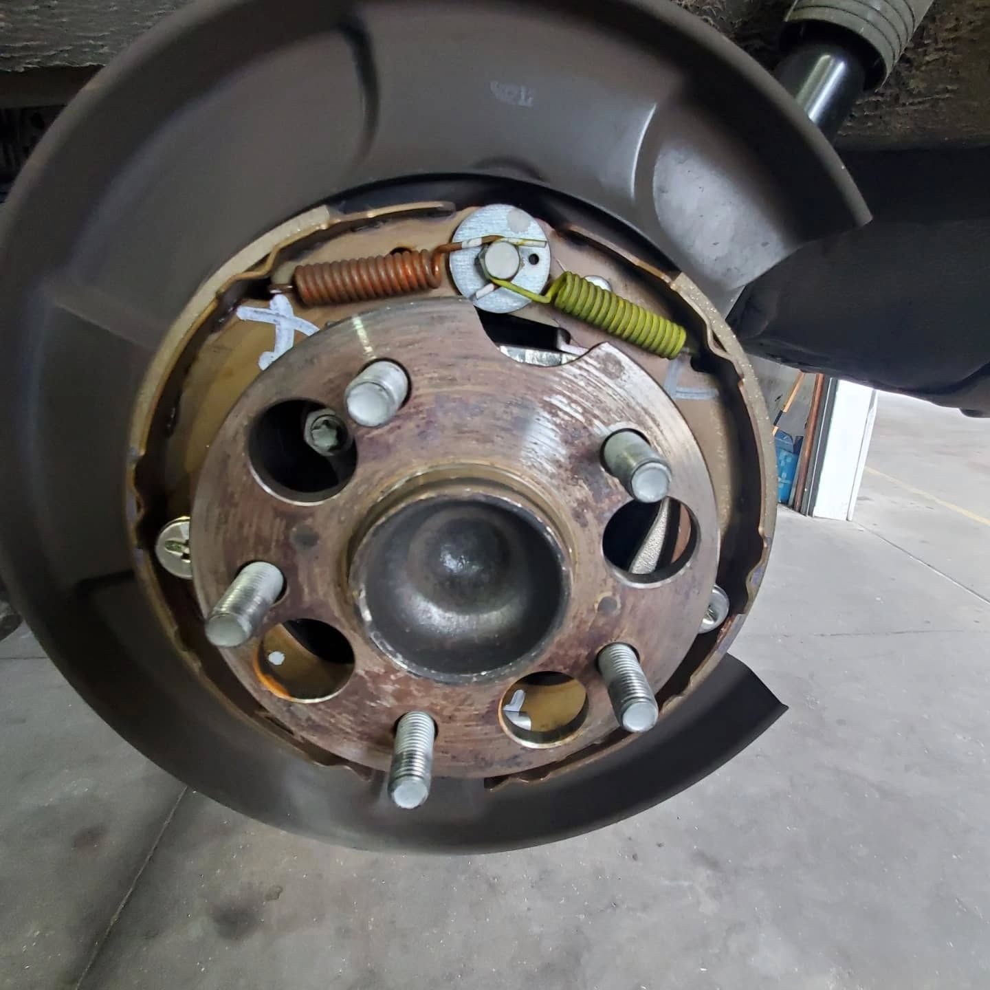 Close-up of a car brake drum and wheel hub with lug studs and suspension springs visible.