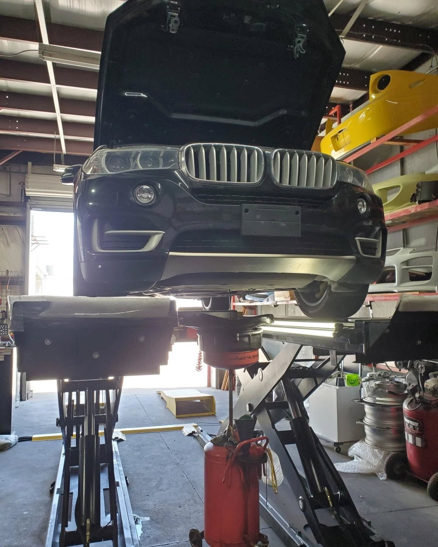 Black SUV lifted on a car repair hoist inside an auto shop with its hood open