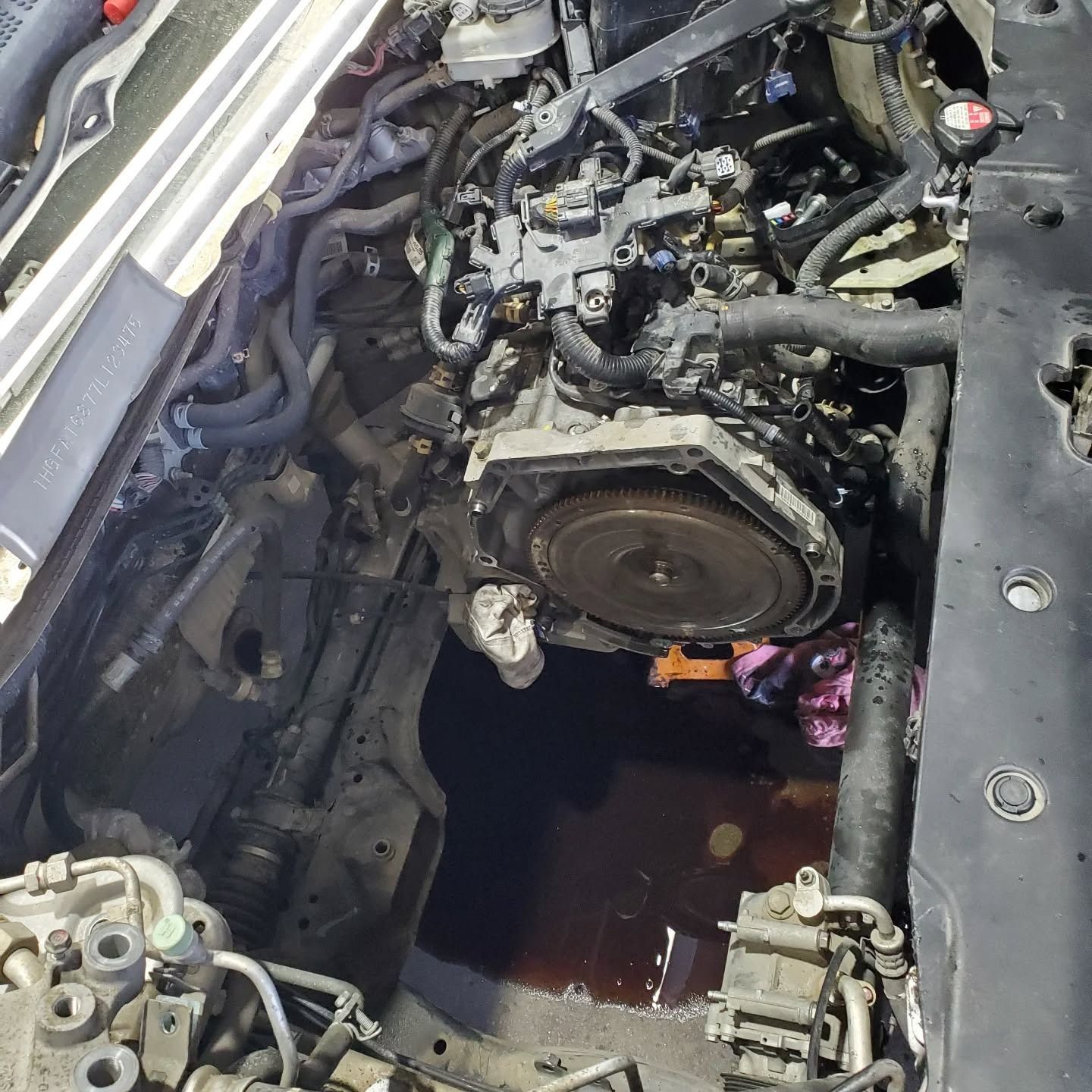 Car engine removed from bay, exposing mechanical parts and a dark fluid puddle below.