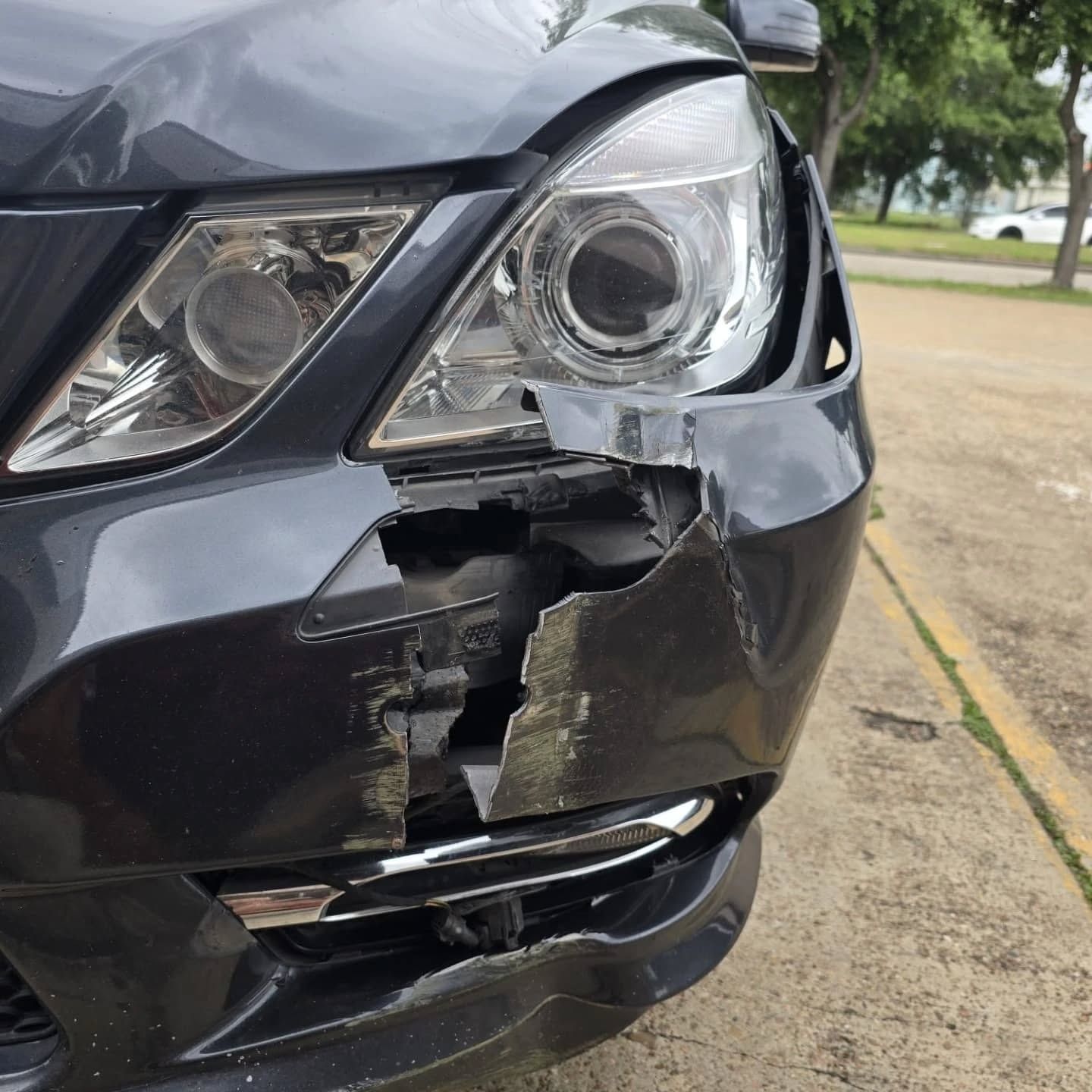 Front-right close-up of a black car with a badly damaged headlight and bumper.