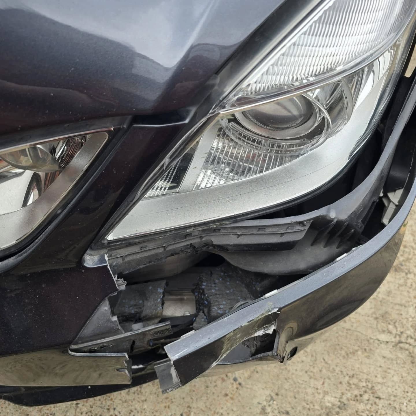 Close-up of a car’s front headlight and bumper with visible collision damage and broken plastic.