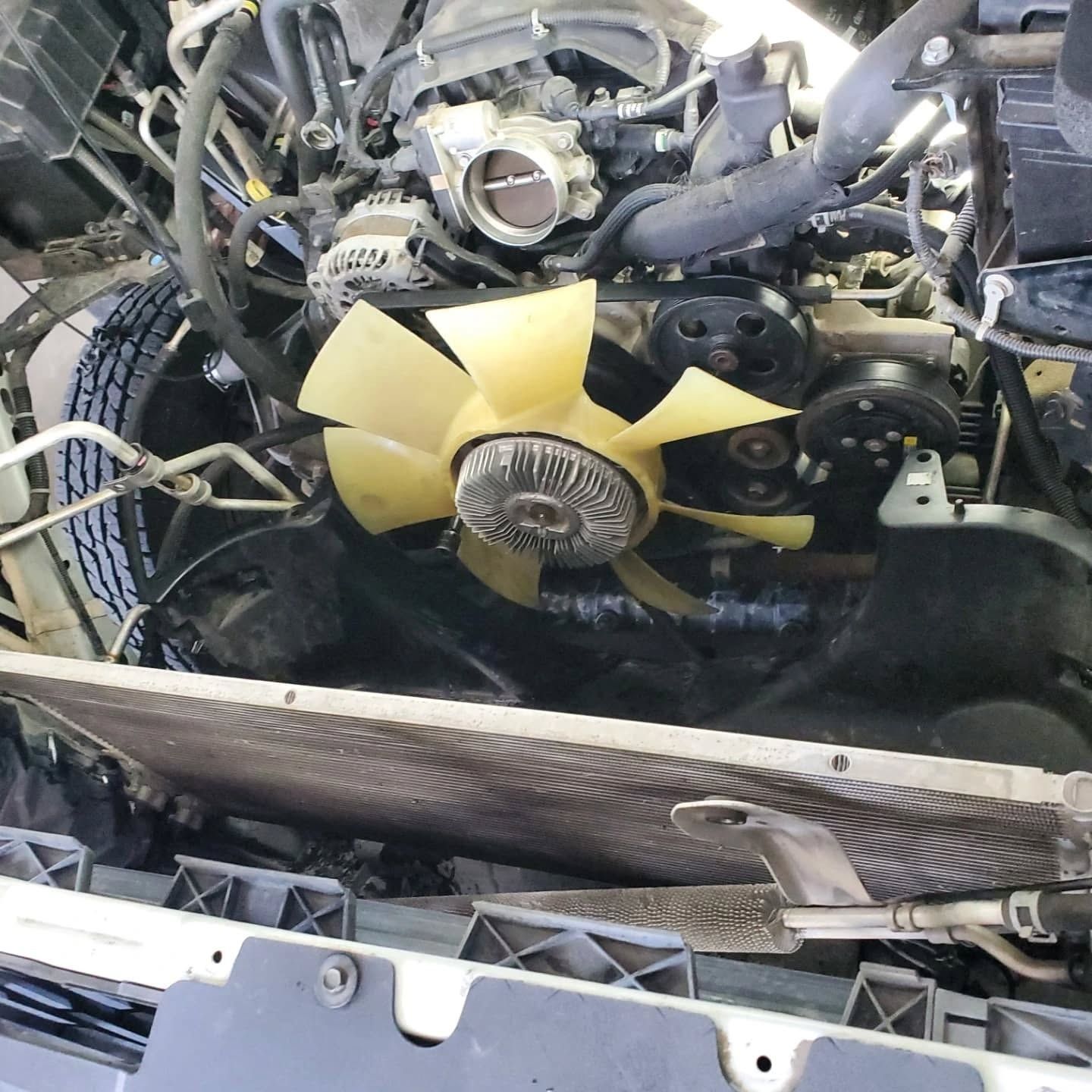 Car engine bay with yellow cooling fan, hoses, and exposed mechanical components.