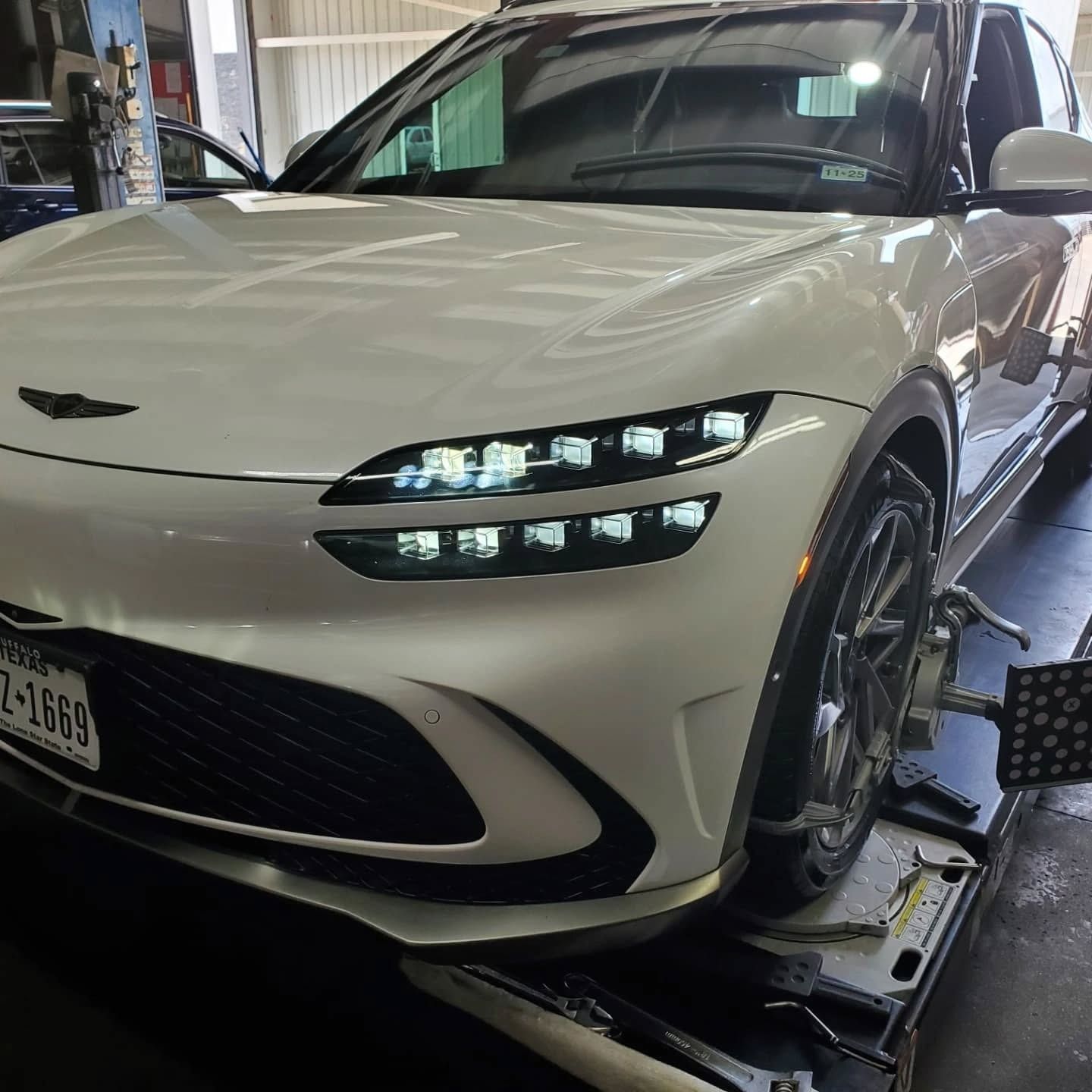 White sports sedan on a lift in an auto shop, front view with headlights on.