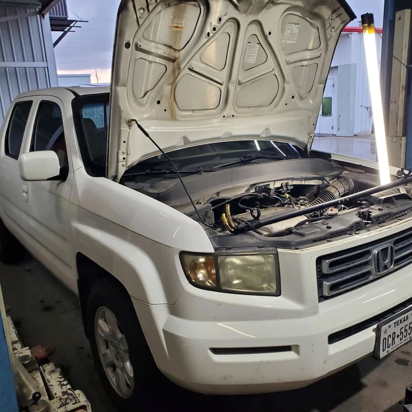 White SUV with hood open in a garage, showing the engine compartment.