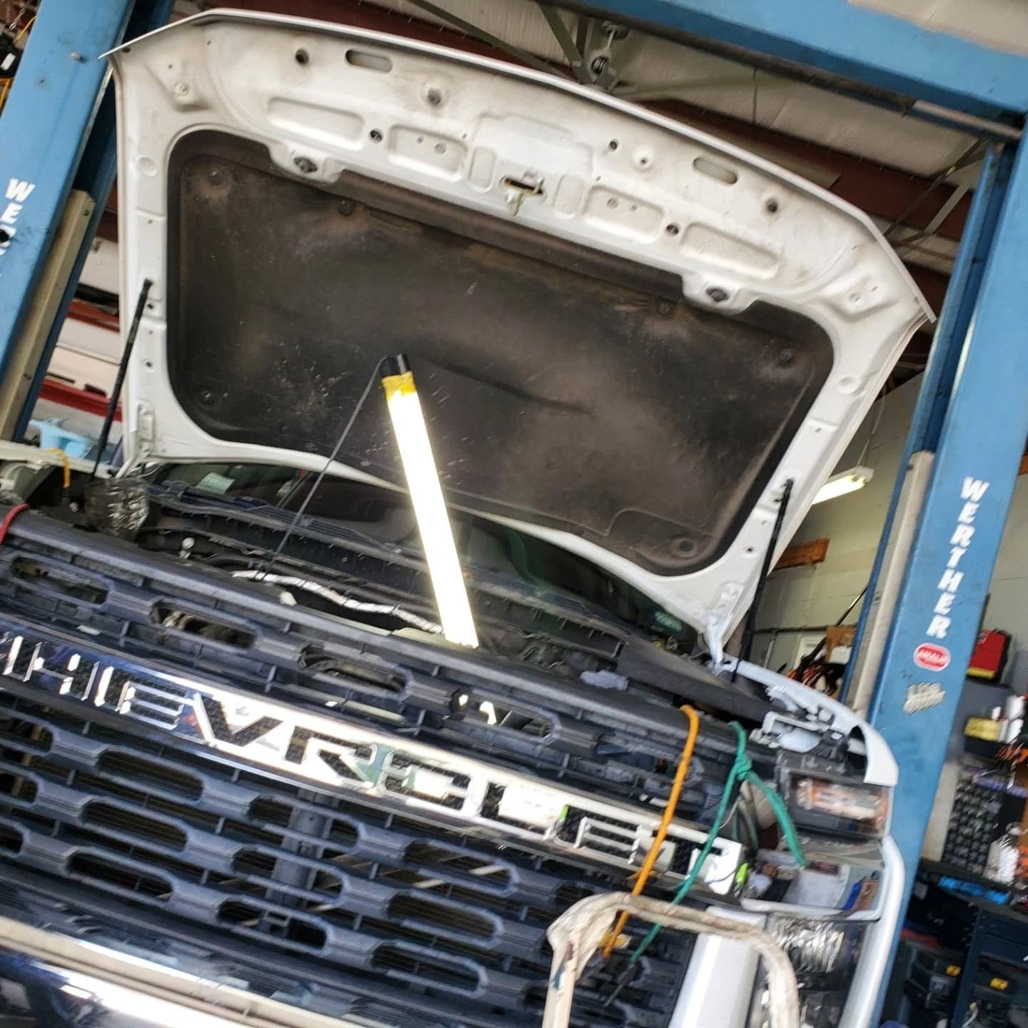 Chevrolet truck in a repair shop with hood open and a work light inside the engine bay