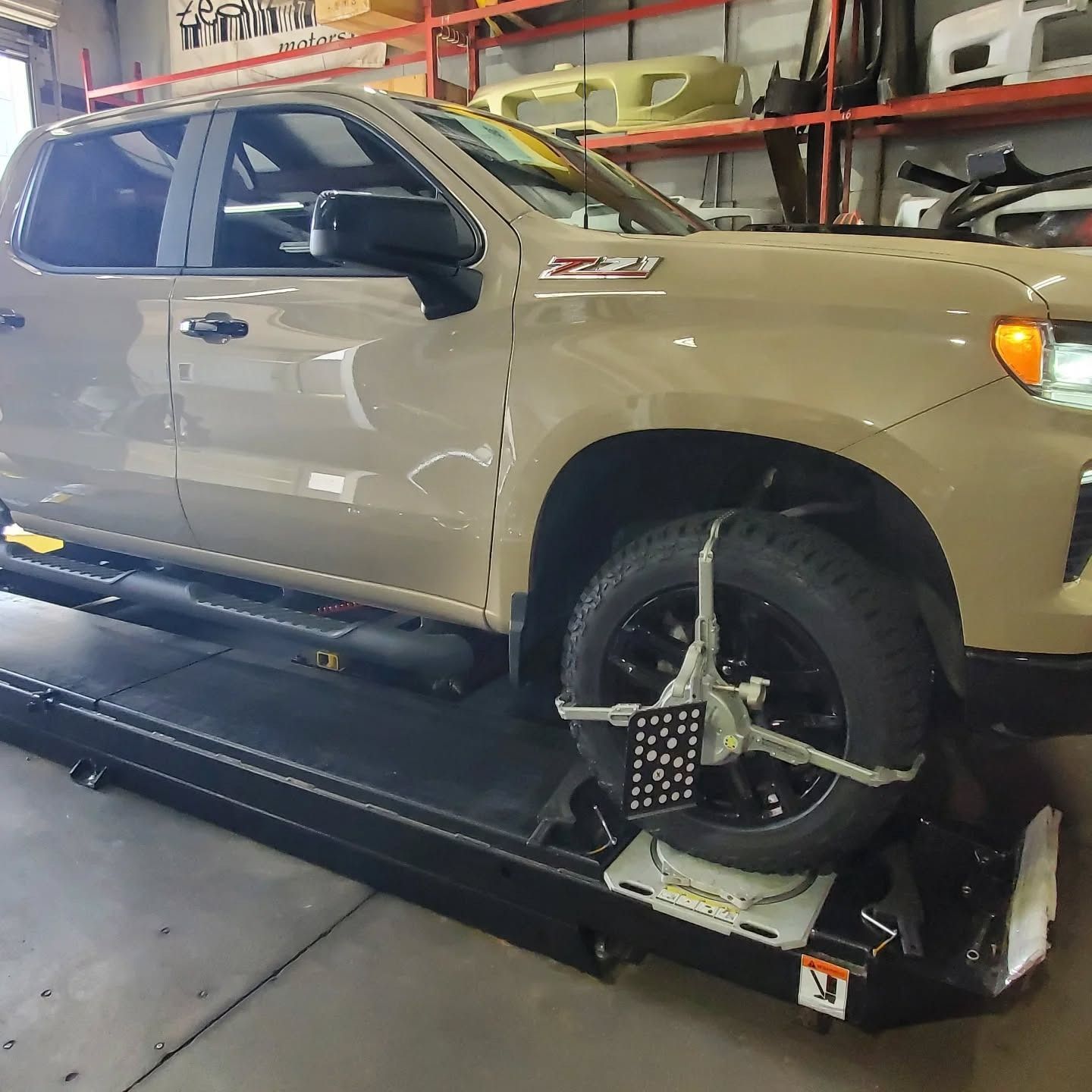 Beige pickup truck on a wheel-alignment machine in an auto shop.