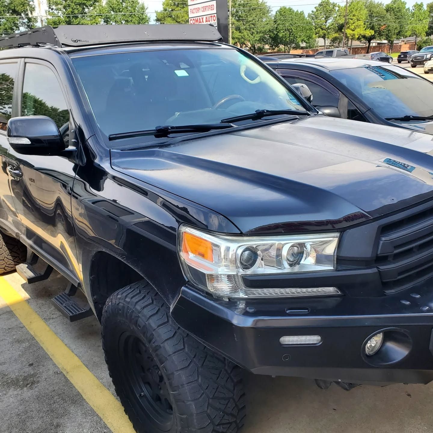 Black SUV parked in a lot, angled front view, with off-road tires and yellow parking lines visible.