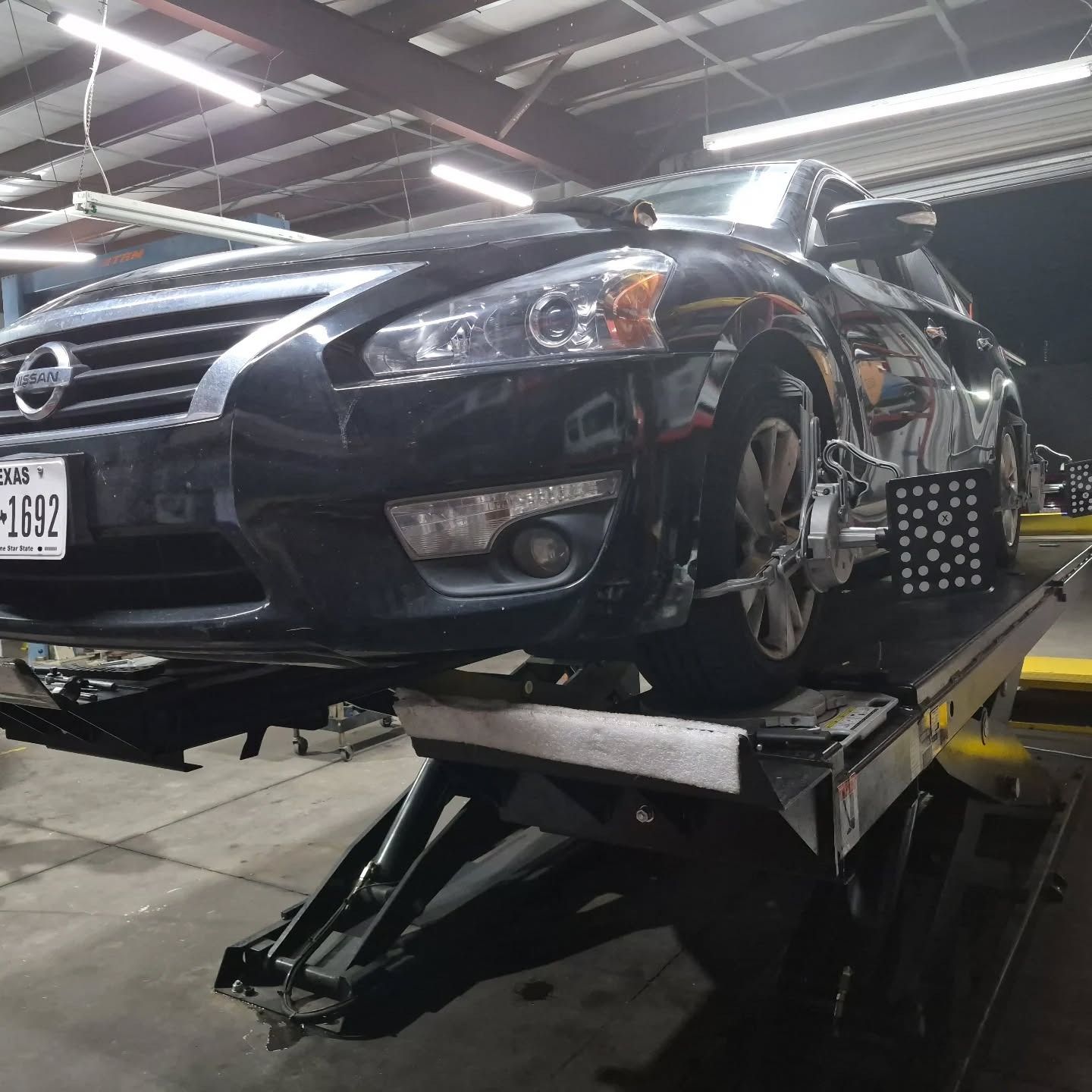 Black sedan on a wheel alignment lift inside a garage, front end close-up with mounted equipment