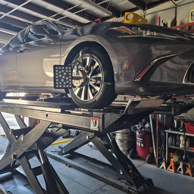 Silver sedan on a raised alignment lift in an auto repair shop.