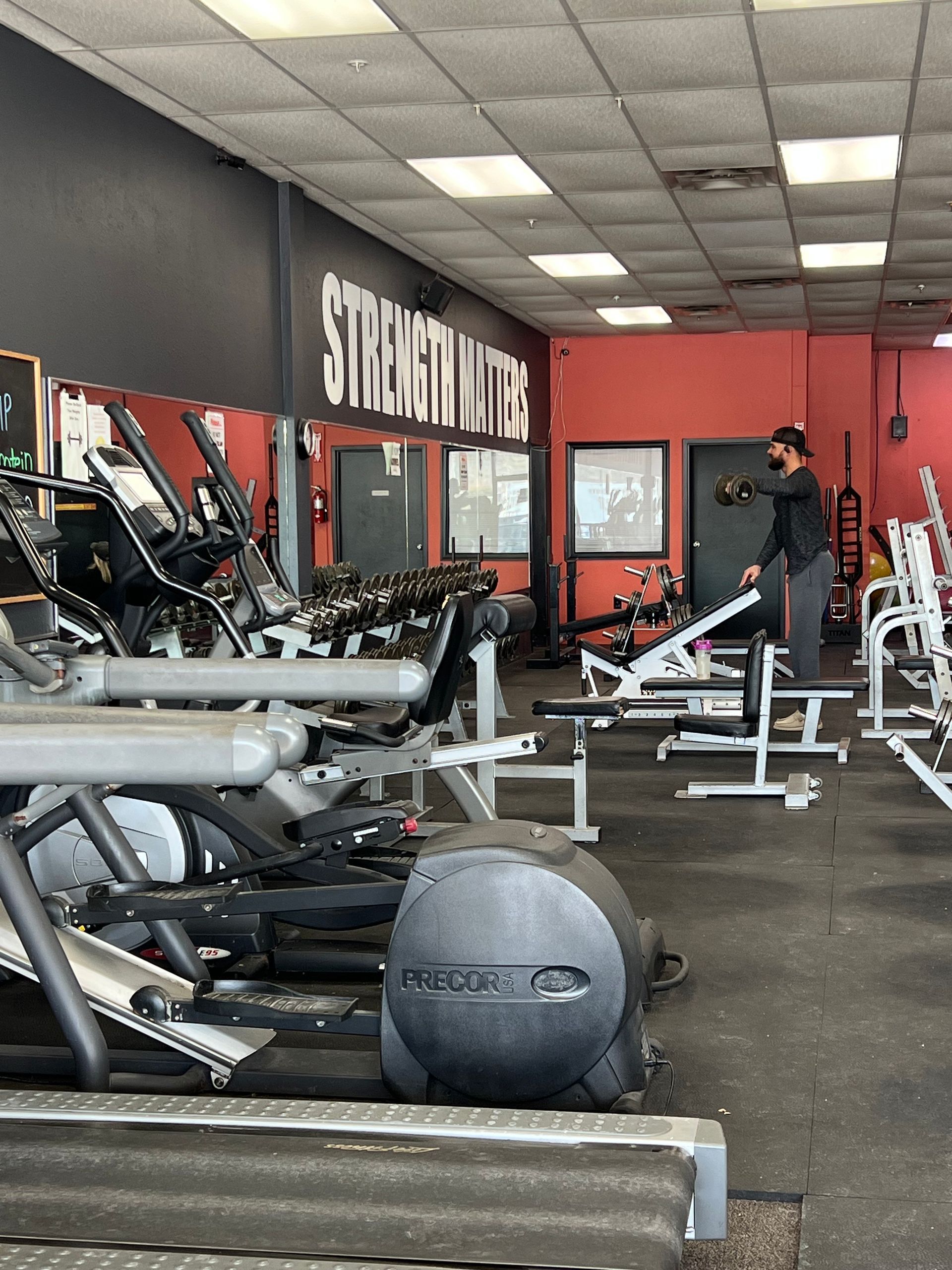 Gym interior with exercise equipment and a person stretching near a weight machine.