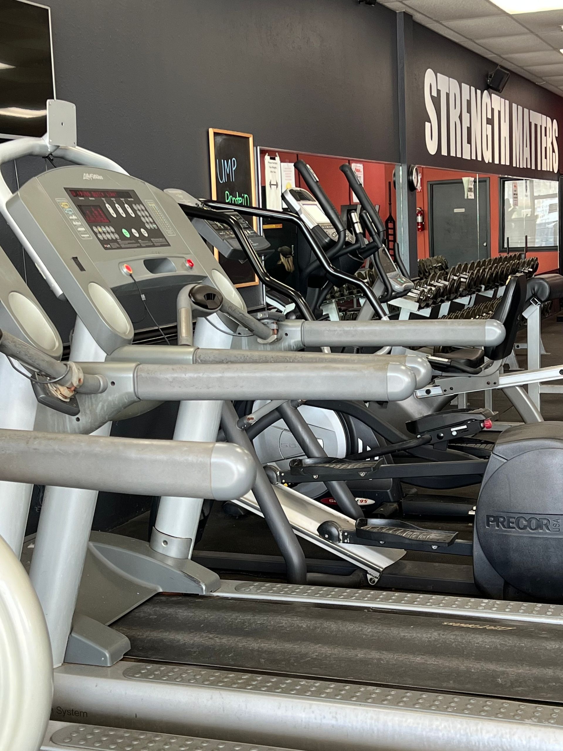 Treadmills and other exercise machines in a gym with dark red and black walls.