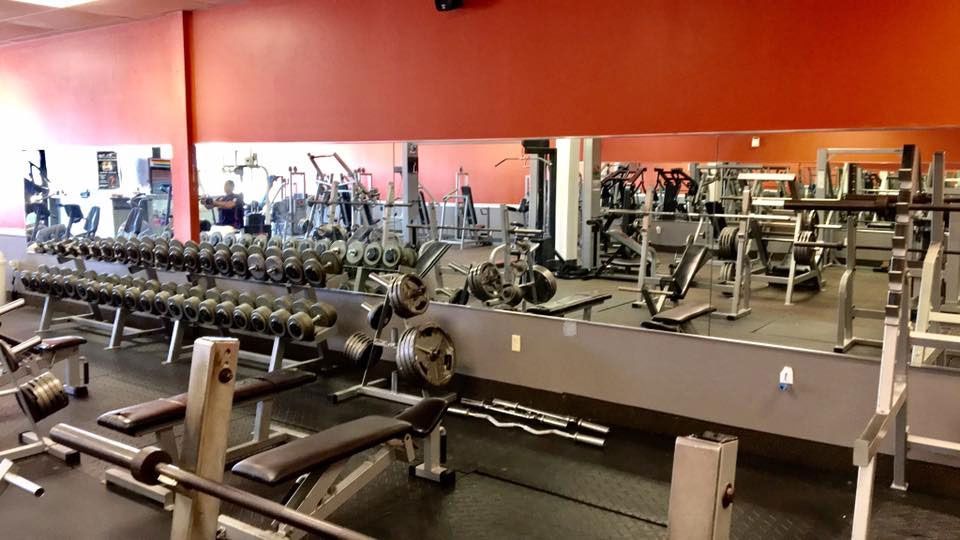 Gym interior with weights, machines, and mirrors. Orange and red walls.