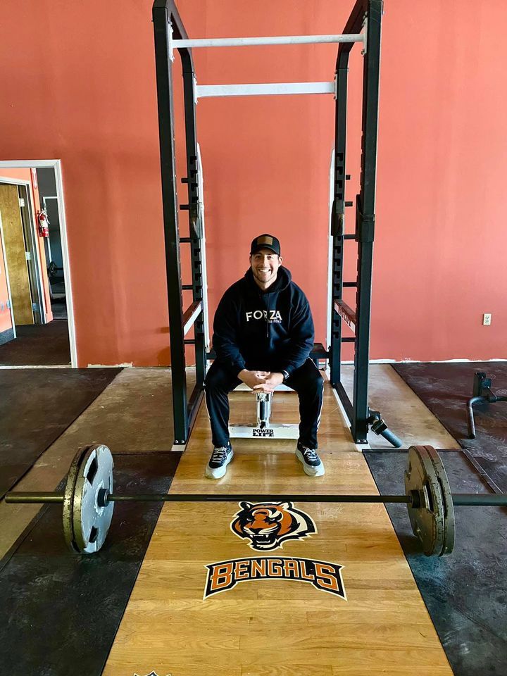 Man sitting in a weight rack with a barbell on a Bengals-themed platform.