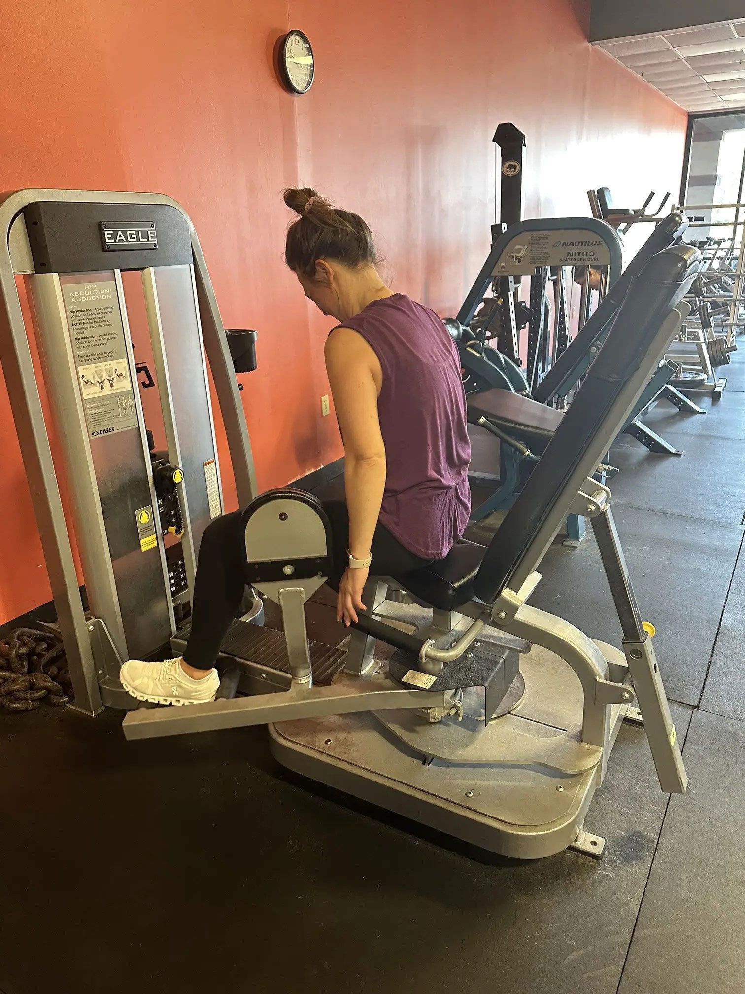 Woman using a leg press machine in a gym, wearing purple top and black leggings.