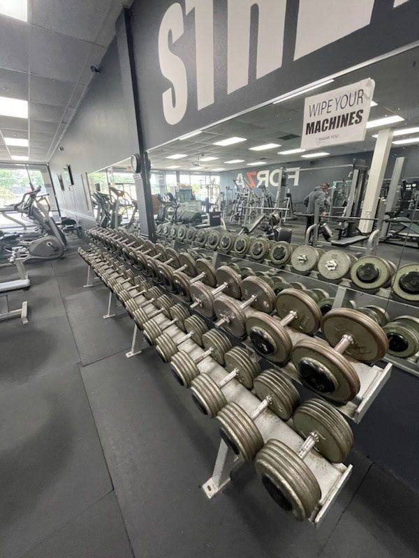 Rows of dumbbells in a gym. Mirrors reflect more weights and workout equipment. 