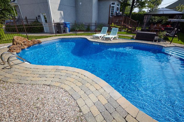 Backyard swimming pool with blue water, stone patio, lounge chairs, and gravel landscaping