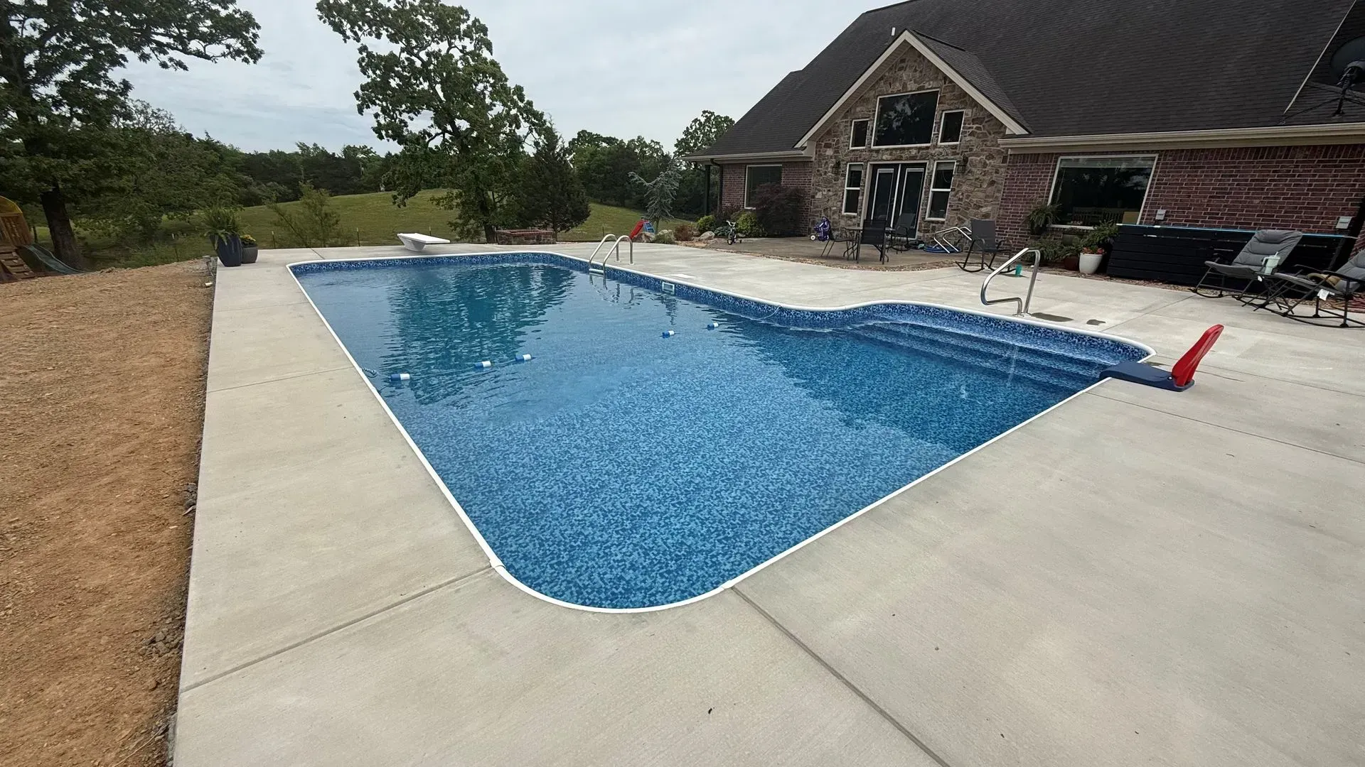 Backyard swimming pool with blue water beside a concrete deck and a brick house