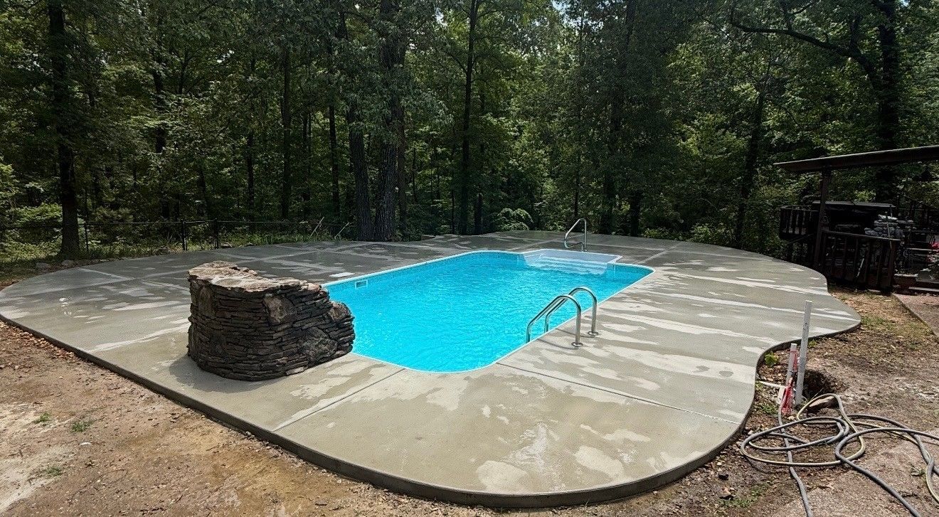 Backyard pool with bright blue water on a concrete deck surrounded by trees