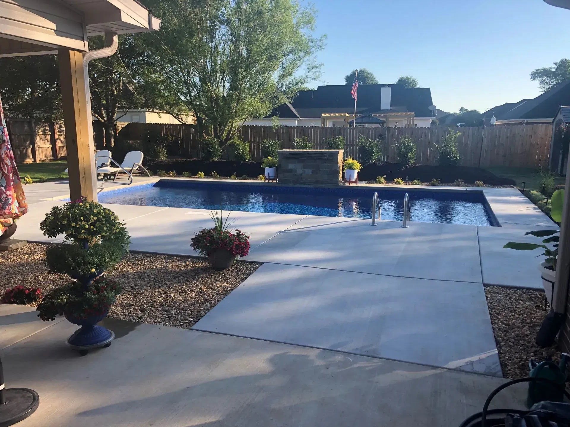 Backyard patio with a swimming pool, potted plants, and trees in bright sunlight