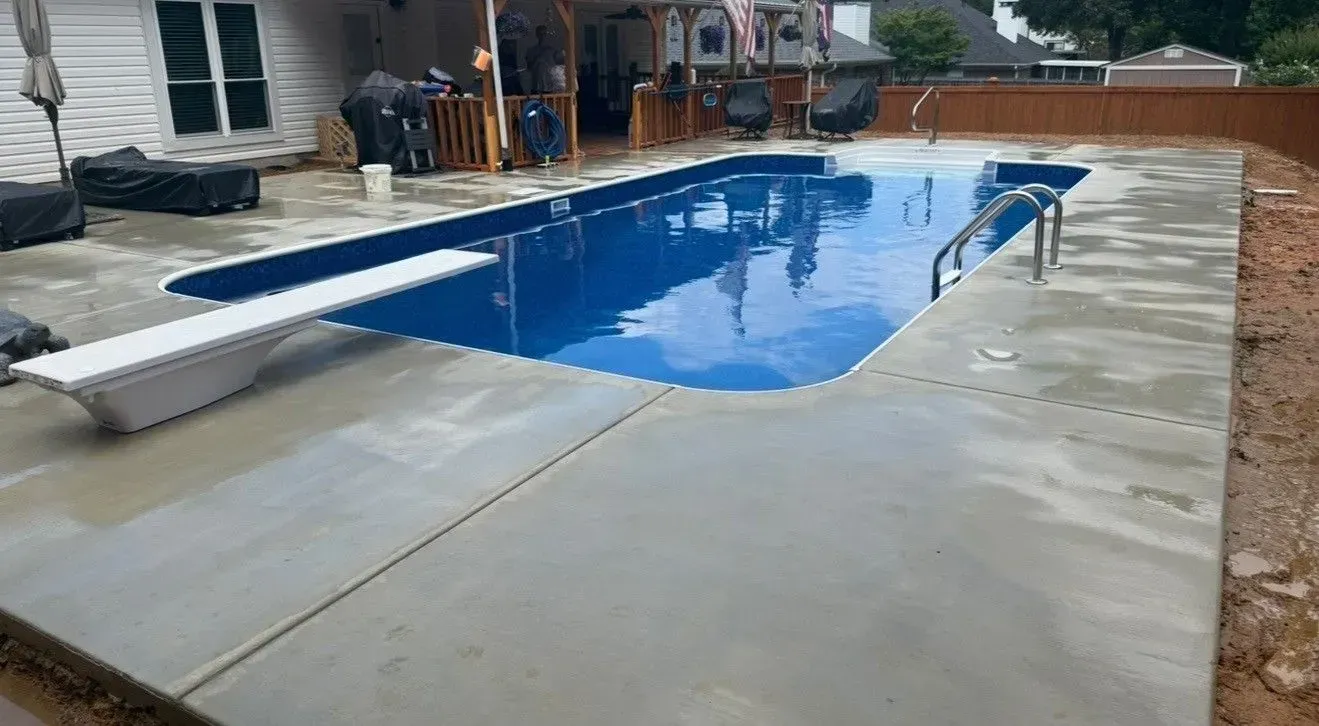 Backyard swimming pool with a wet concrete deck and a diving board on the left.