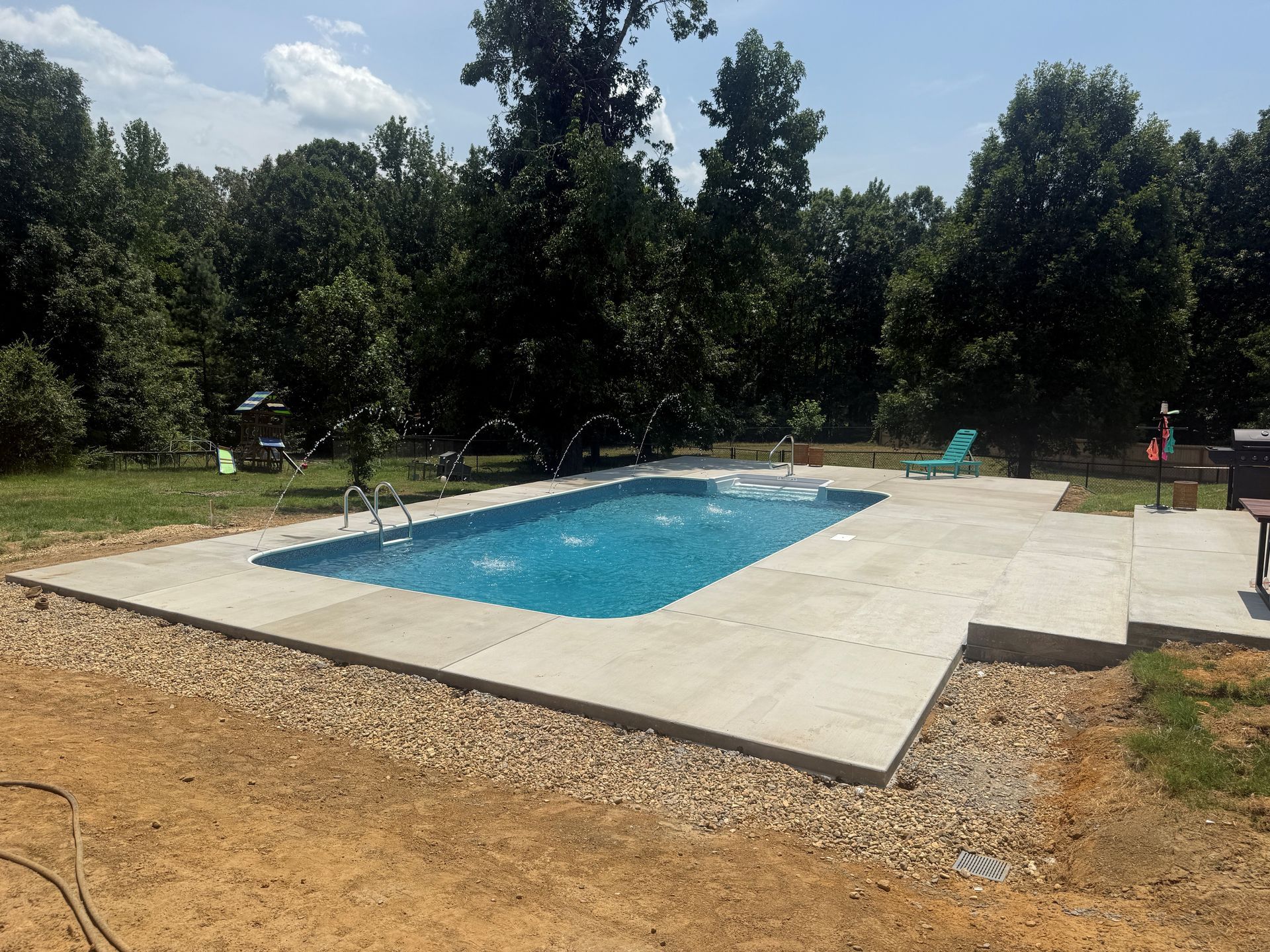 Rectangular backyard pool with blue water, pale deck, and trees surrounding it