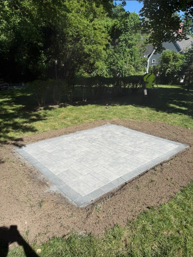 Concrete slab in a grassy yard, bordered by dirt and trees in the background.