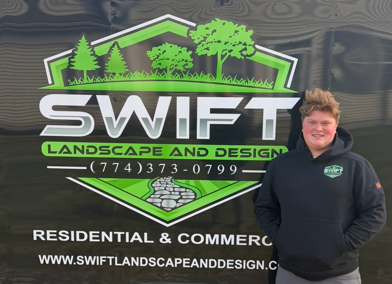 Person operating orange lawn mower on a green lawn, wearing a black hoodie and baseball cap.