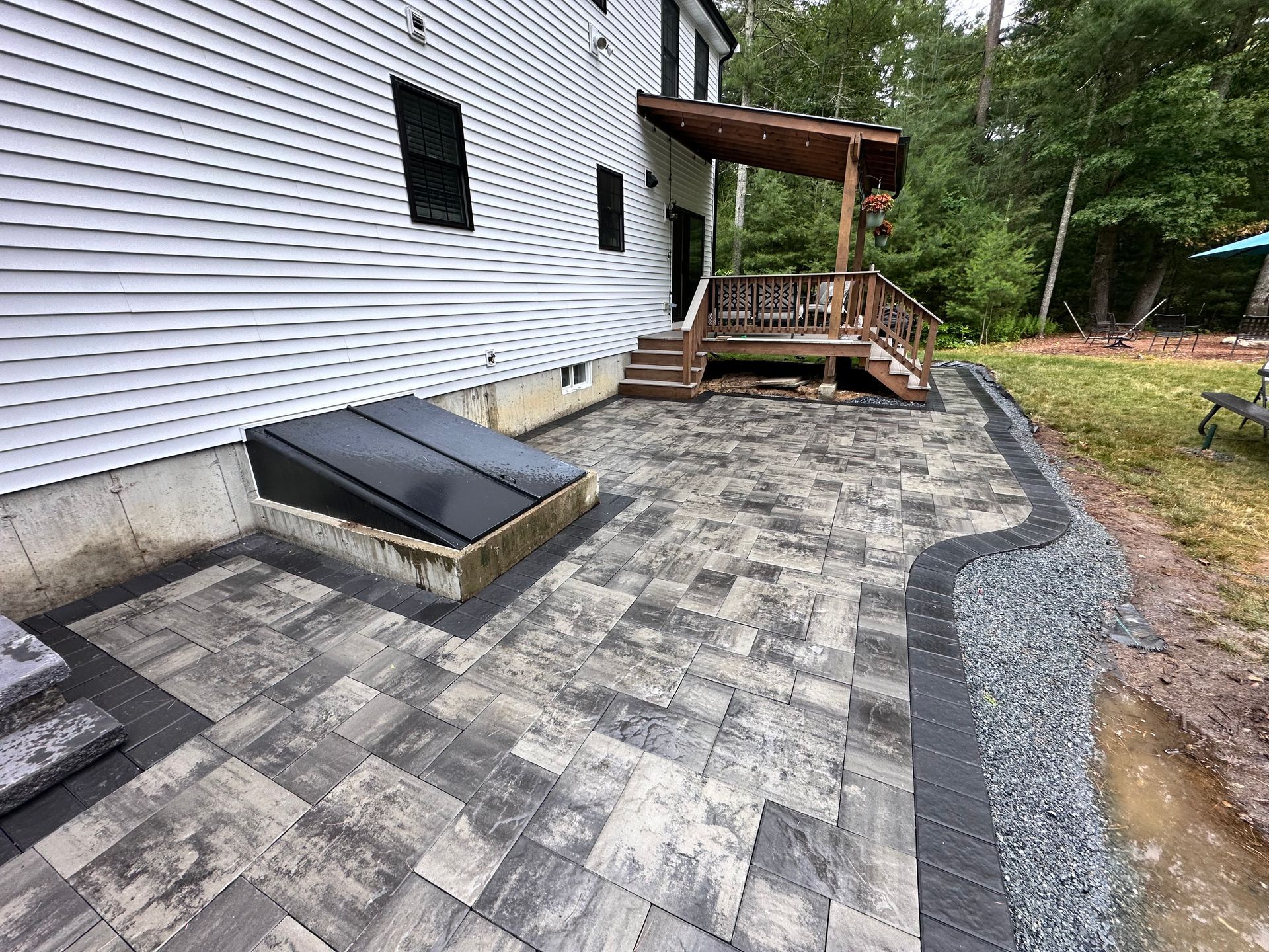 Patio with pavers and retaining wall next to a house with a door and deck.