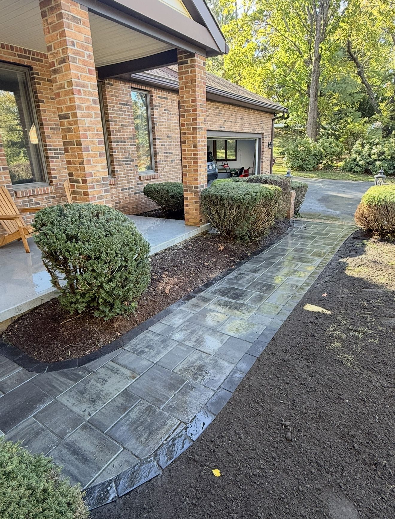 Brick home entrance with paved walkway, garden beds with shrubs.