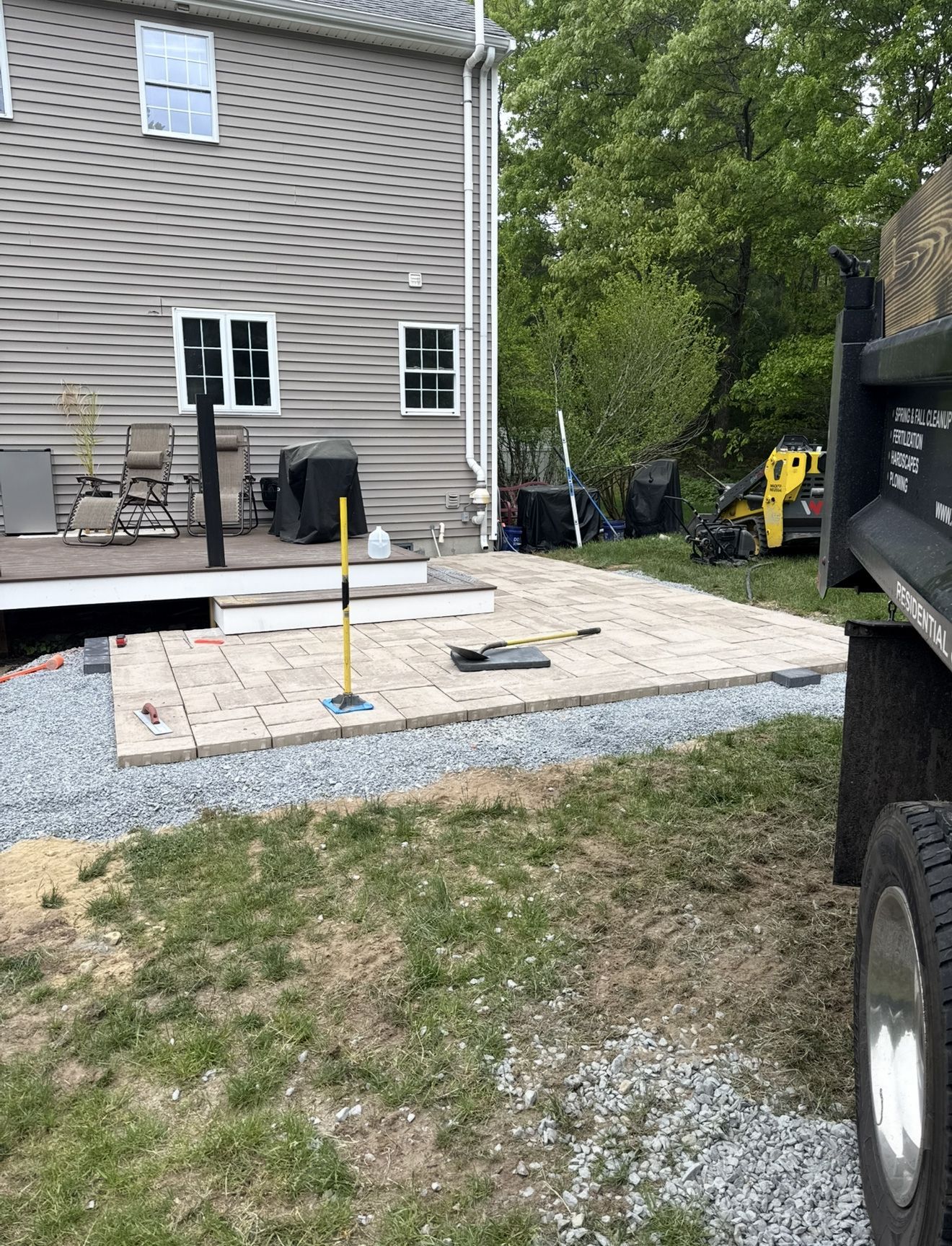 Patio construction: paving stones laid on a gravel base next to a house. A truck is parked to the right.