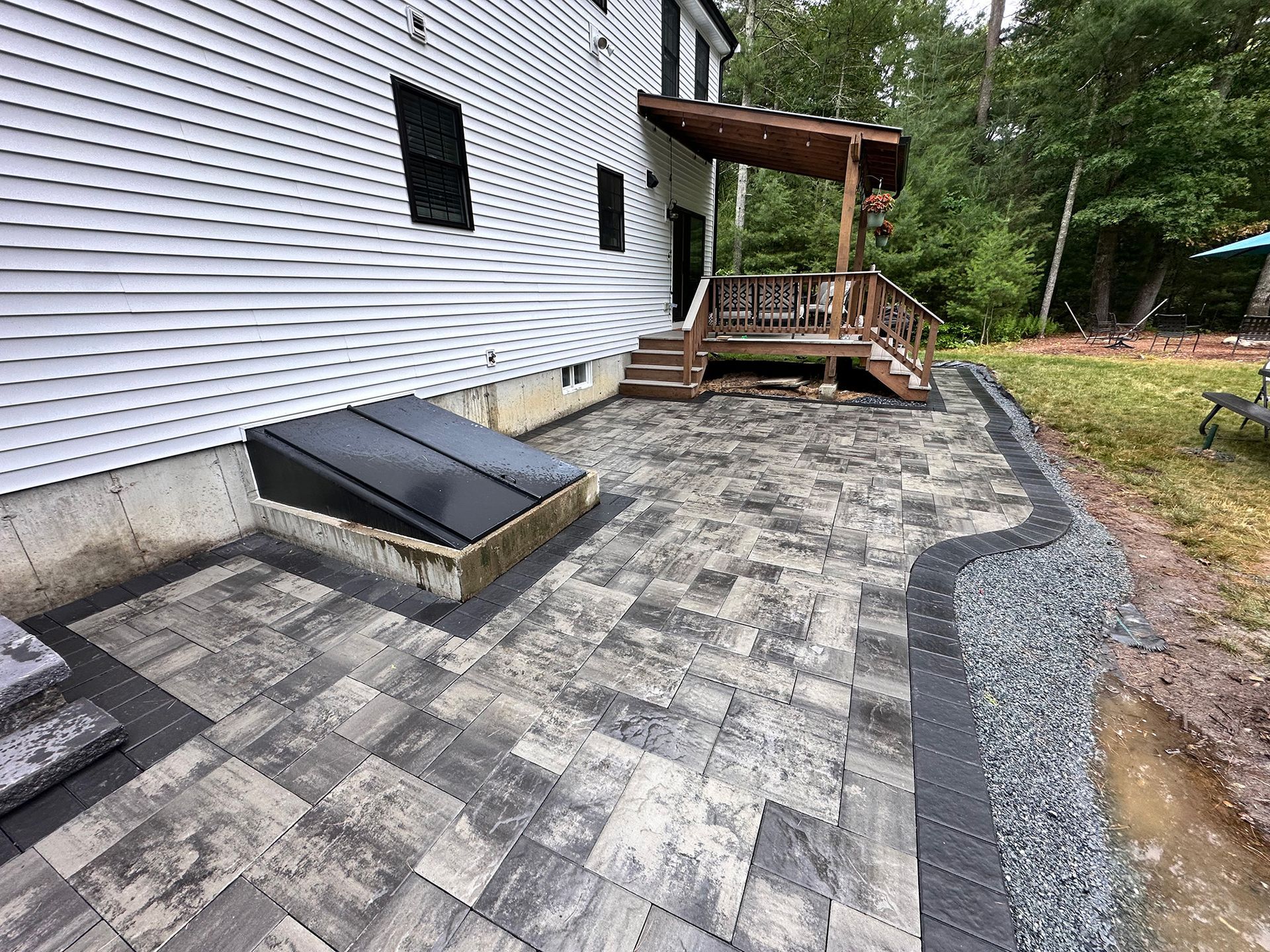 Backyard patio with patterned pavers, a retaining wall, and a raised wooden deck.
