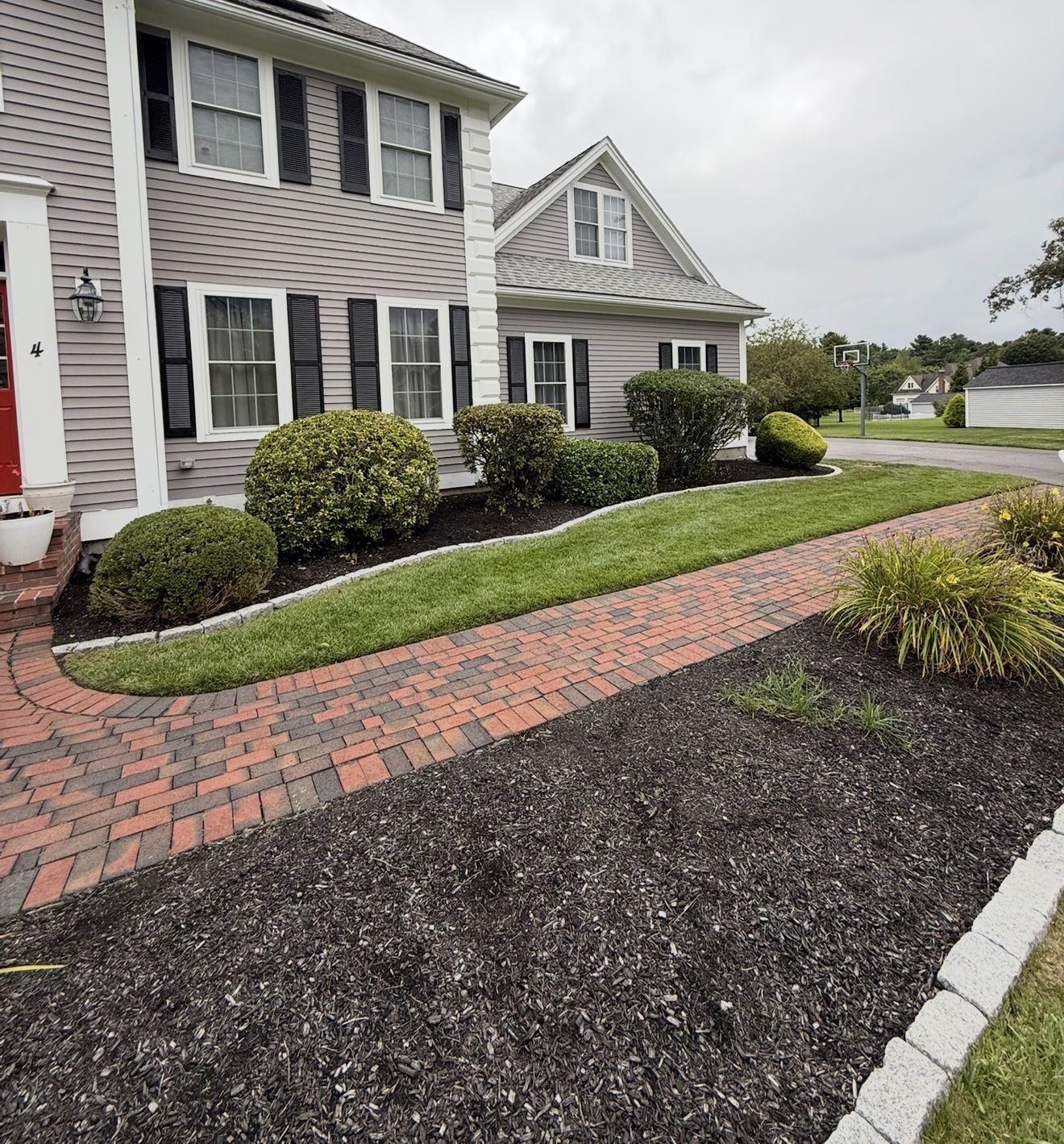 A two-story house with a brick walkway and well-manicured landscaping in front.