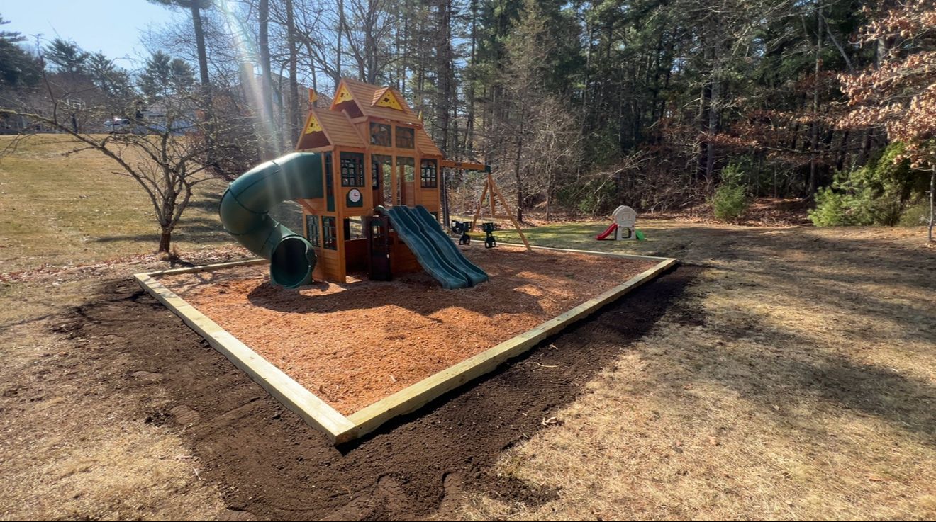 Playground with wood frame and mulch base. A slide and tunnel lead from wooden structure on a sunny day.