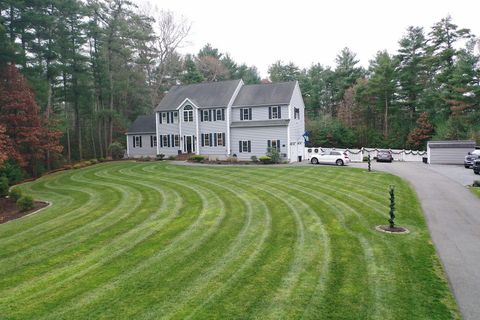 Two-story gray house with green lawn featuring curved mowing patterns. Cars in driveway and surrounding trees.