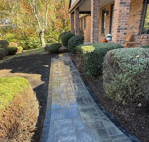A brick home with a stone walkway lined with trimmed bushes.