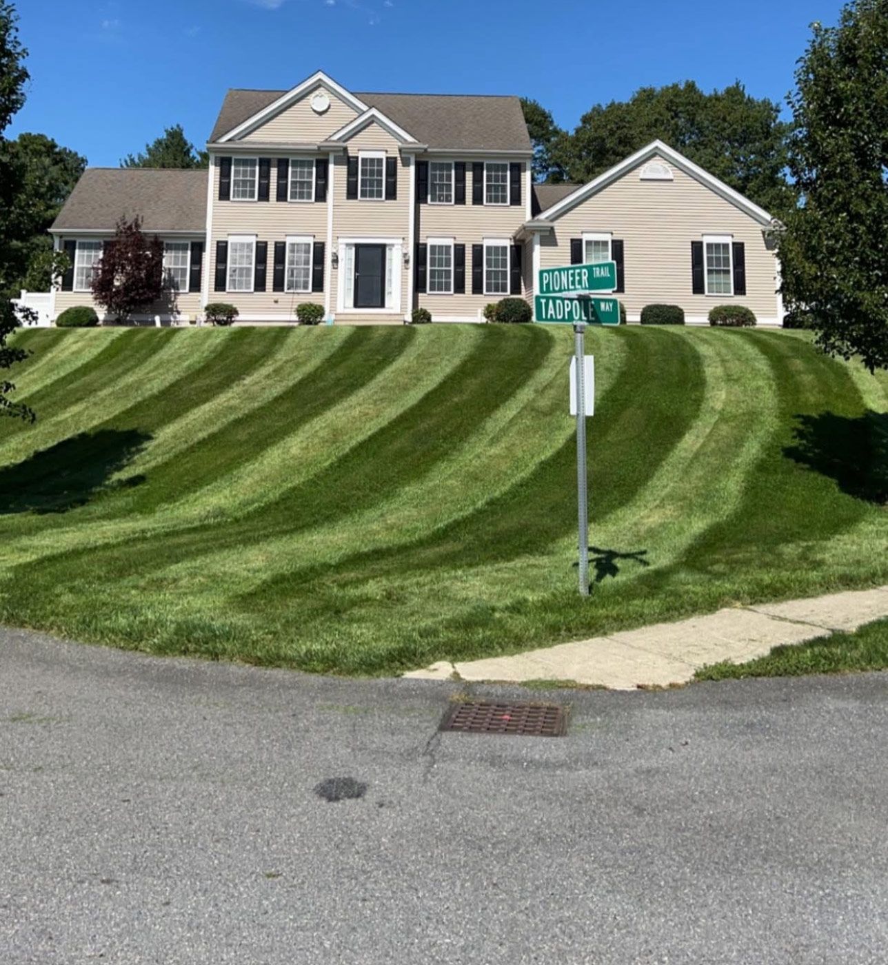Two-story house with striped lawn; street corner with street signs.
