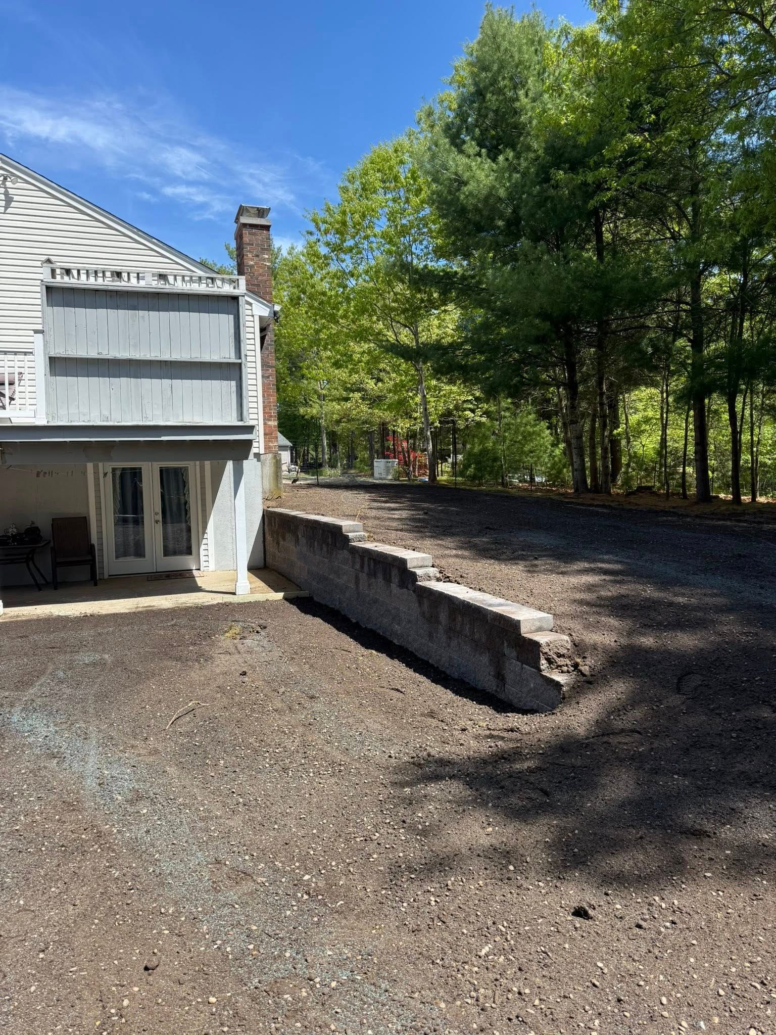 Backyard with retaining wall, house, and trees on a sunny day. Ground covered in dark mulch.