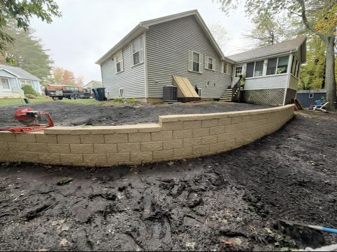 A backyard with a newly built curved retaining wall and a house in the background. Muddy ground.