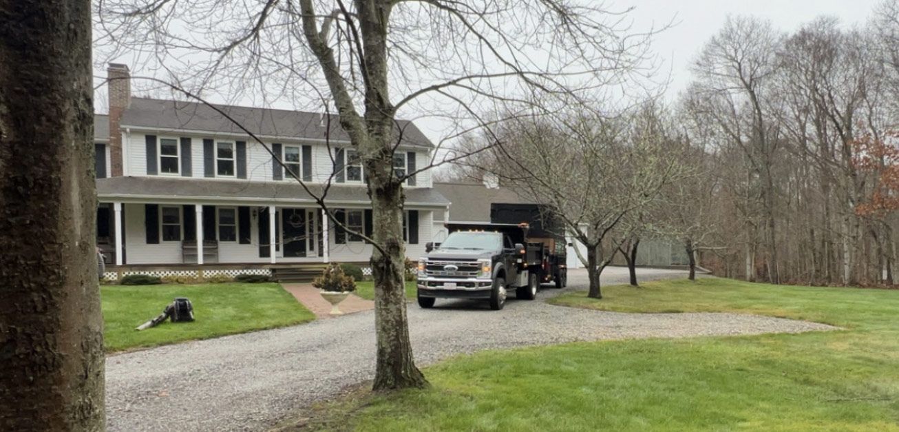 A white two-story house with a black-bed truck parked in front of it on a gravel driveway.