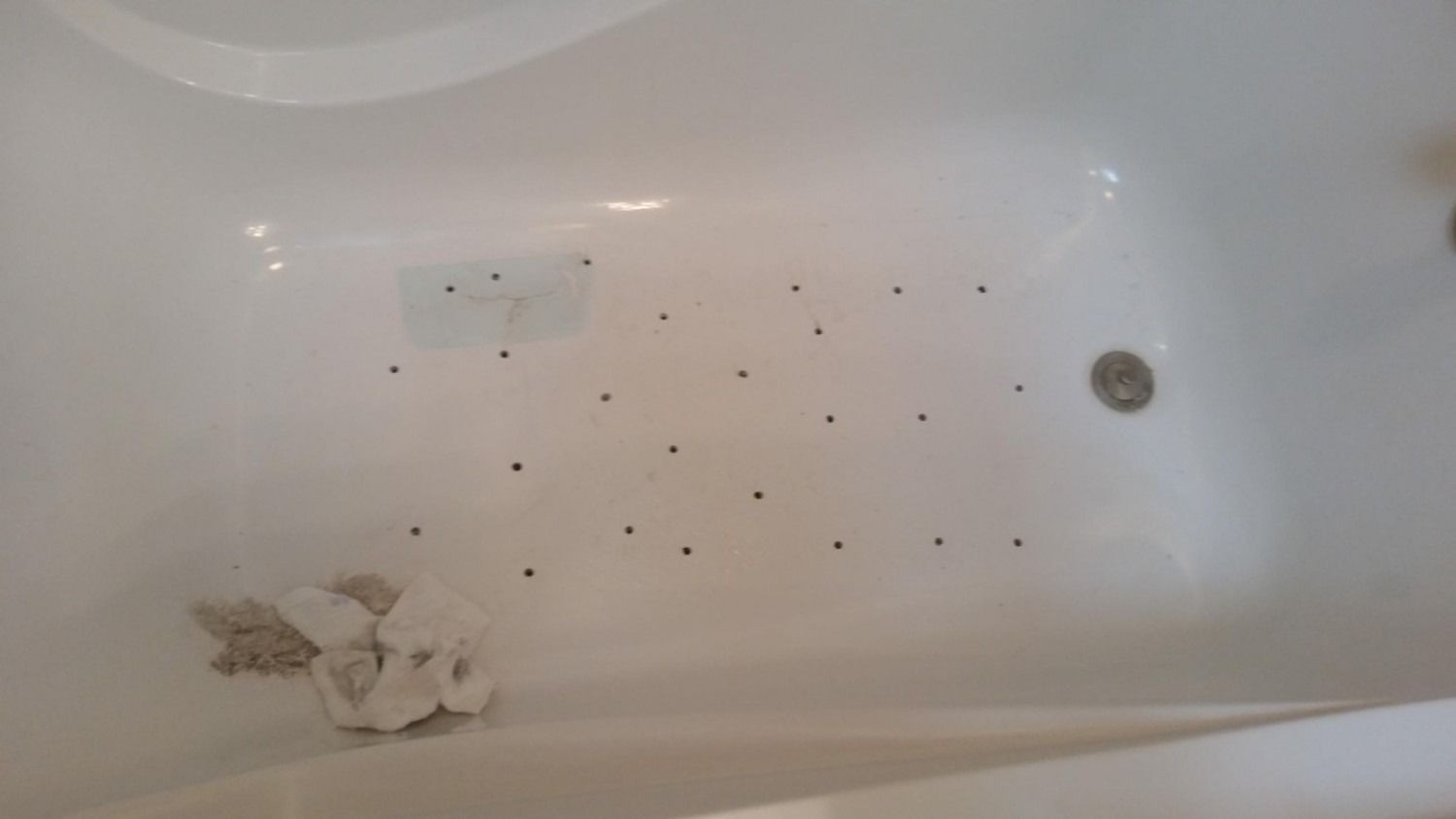 White bathtub with scattered black specks and a small pile of tissue or debris near the drain.