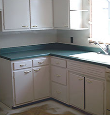 Small kitchen corner with white cabinets, teal countertop, and a sink by a bright window