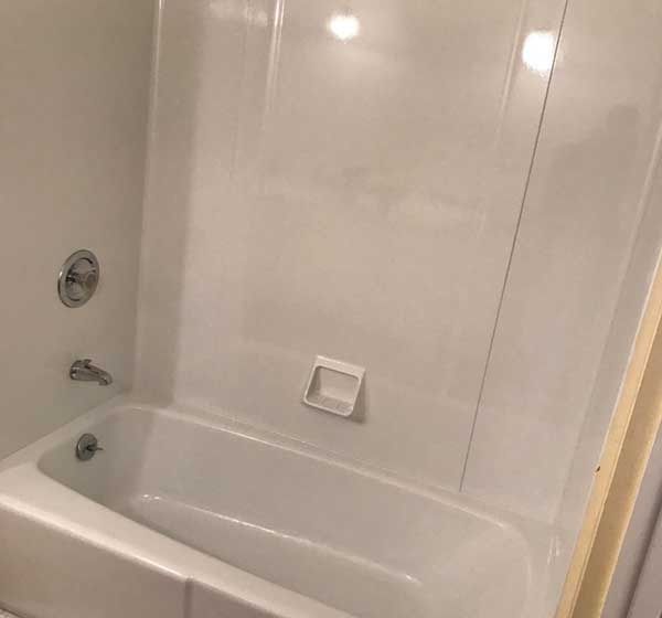 White bathtub and shower surround with built-in soap shelf and chrome fixtures