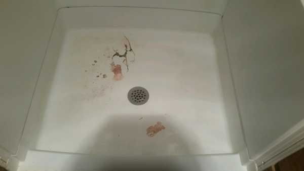 Dirty white shower floor with a drain and reddish stains.