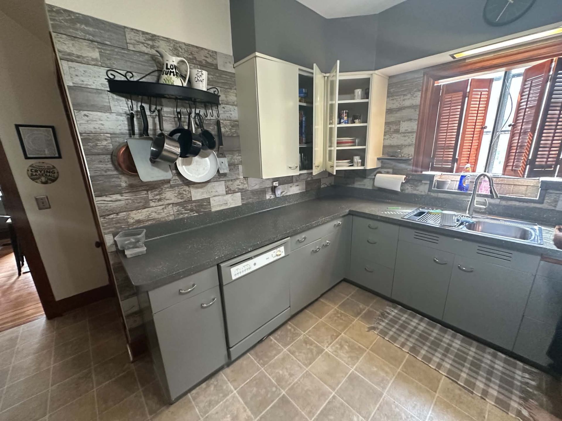 Modern kitchen with gray cabinets, black countertops, hanging pots, and a bright window over the sink.