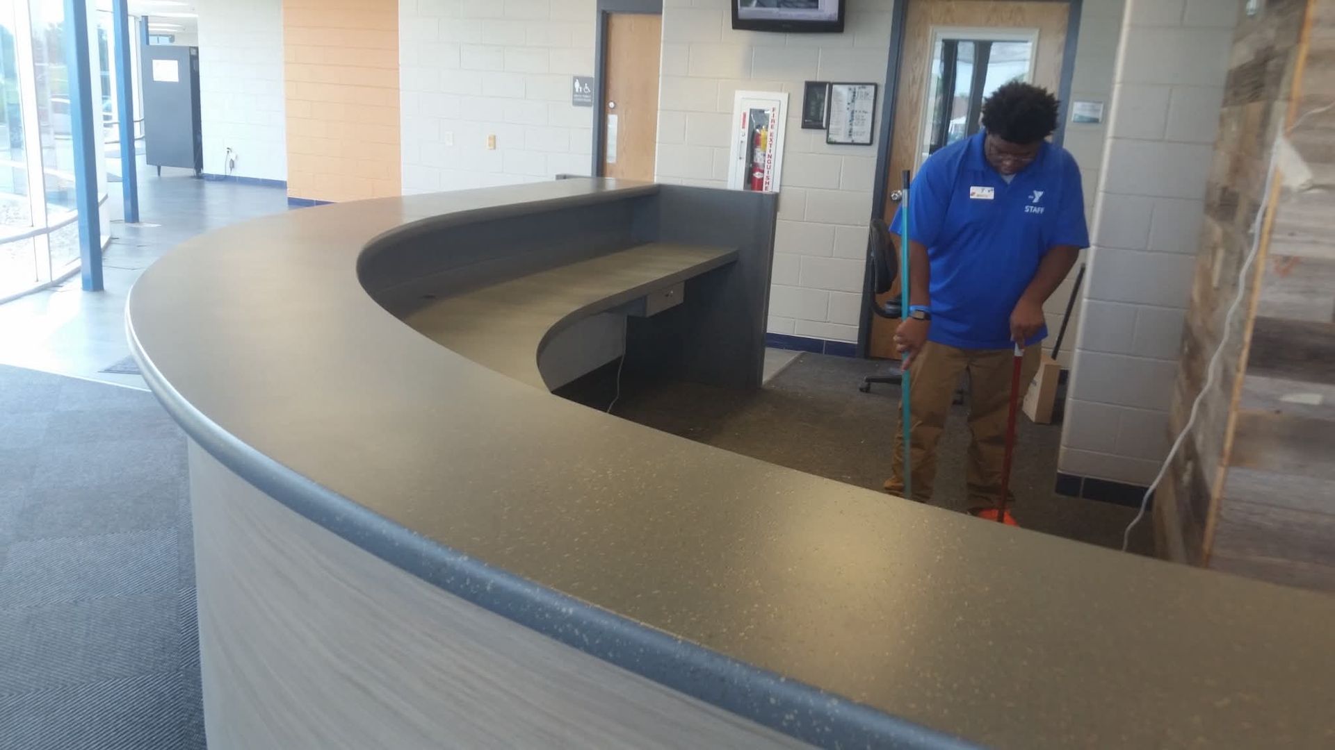Curved reception desk in a lobby, with a person in a blue shirt standing behind it.