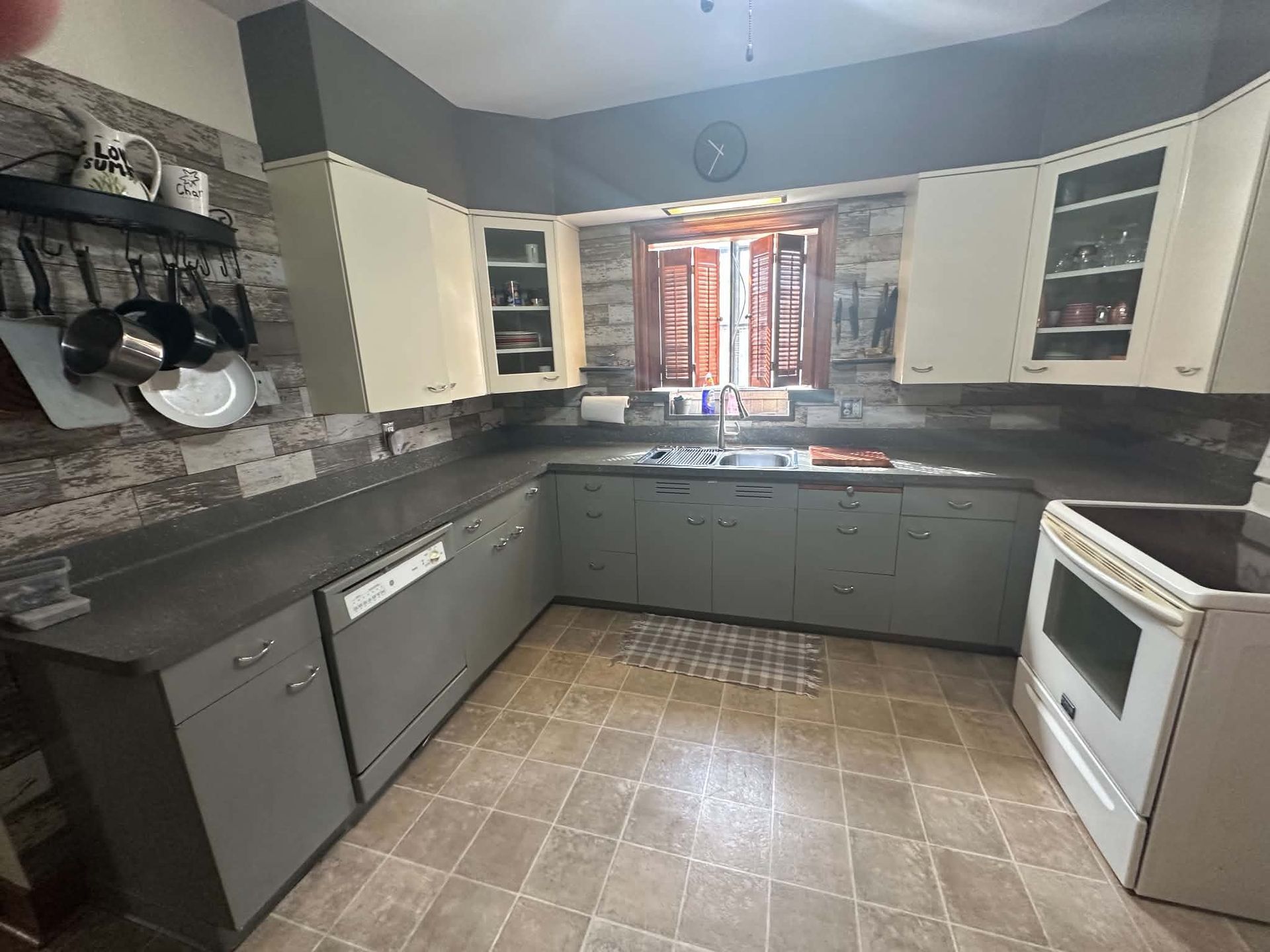 Modern kitchen with gray cabinets, black countertop, white appliances, and a window over the sink.